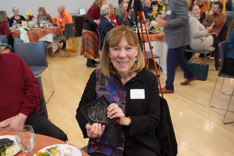 Lynn Scheller wearing a black blouse holding a crystal heart award