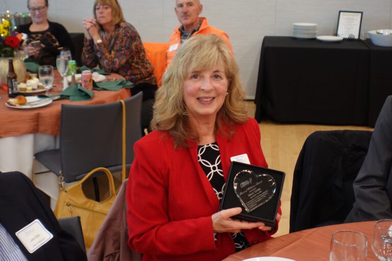 Mary Ordal wearing a red blazer holding a crystal heart award